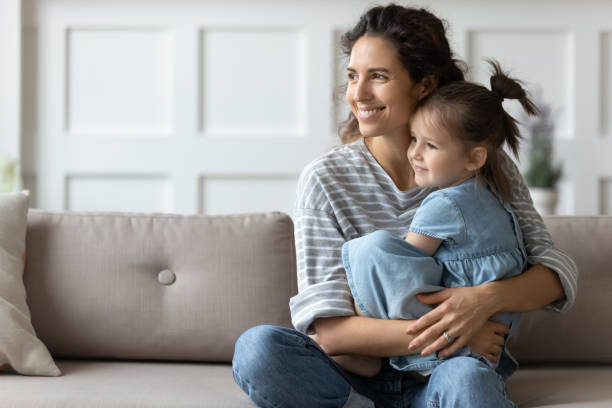 istock Dreamy affectionate curly mother cuddling small preschool daughter, looking away. 1207723169