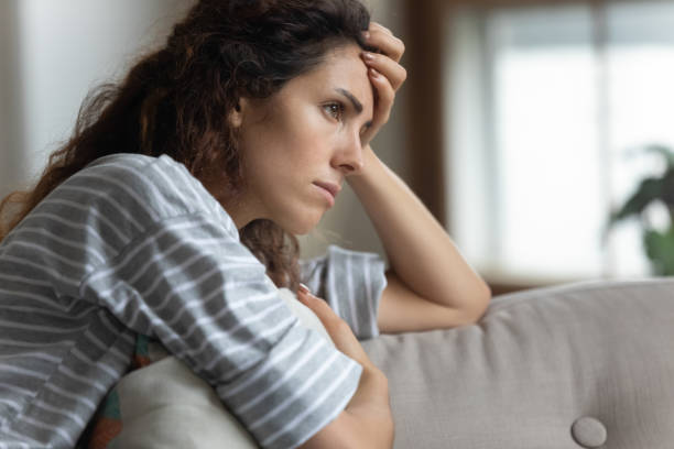 Nervous woman looking away, lost in thoughts alone at home. Side view head shot close up unhappy worried woman sitting on couch, touching forehead, feeling desperate, thinking of problems. Nervous young lady looking away, lost in thoughts alone in living room. pessimism photos stock pictures, royalty-free photos & images