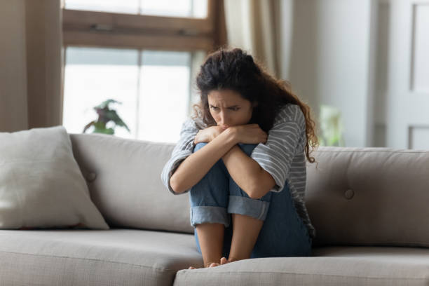 Stressed young woman embracing knees, sitting alone on couch.
