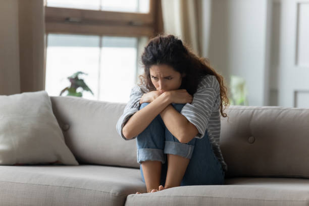Stressed young woman embracing knees, sitting alone on couch. Stressed young woman embracing knees, sitting alone on couch in living room, feeling depressed. Unhappy desperate millennial curly lady regretting of decision, thinking of personal problems at home. pessimism photos stock pictures, royalty-free photos & images
