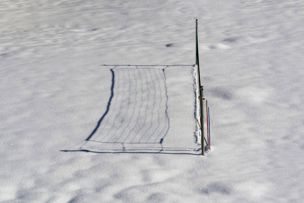 A volleyball pitch is heavy covered with fresh snow. A volleyball net shadows on snowdrifts. Snowy weather in winter. Snow sparkles in the bright sunlight.