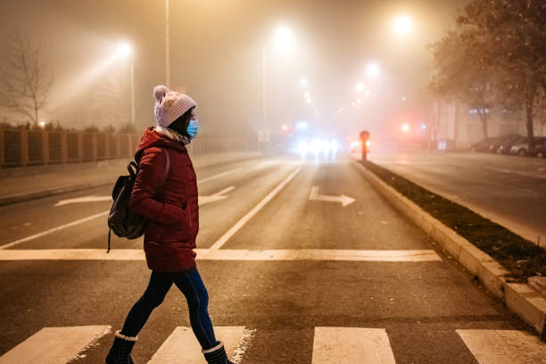 donna con maschera che attraversa strada - global warming smog city pollution foto e immagini stock