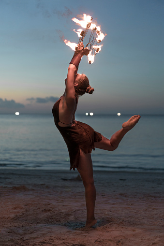 Beautiful, young woman performing fire dance on the beach.