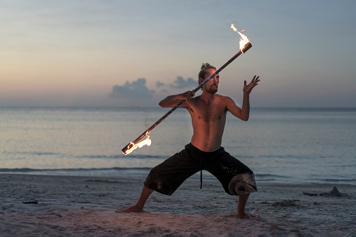 Young man performing fire dance with a flaming torch on the beach.