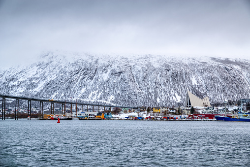Tromso, Norway - february 11, 2020 : Port and harbour with famous Tromso Bridge across Tromsoysundet strait in the background