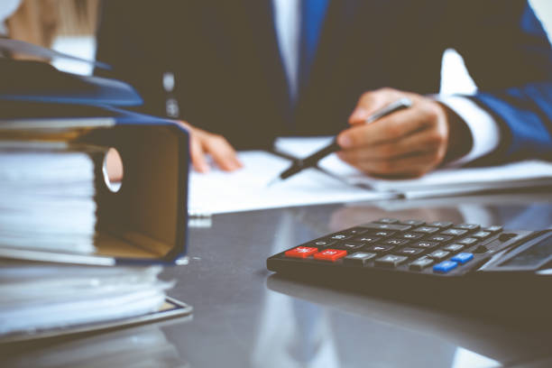istock Binders with papers waiting to be processed with businessman or bookkeeper back in blur. Accounting planning budget. Audit, insurance and business concept 1207727587