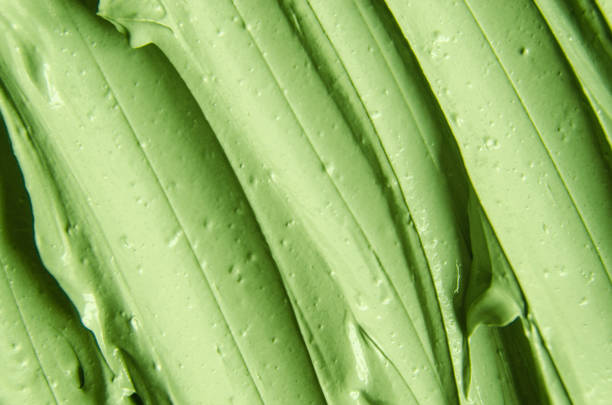Green cosmetic clay (cucumber facial mask, avocado face cream, green tea body wrap) texture close up, selective focus. Abstract background with brush strokes