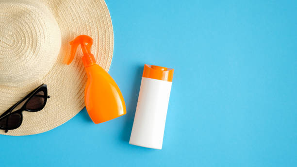 istock Blank sunblock spray package and sunscreen lotion bottle on blue background with sunglasses and beach hat. Top view with copy space. Sun protection cosmetic products, summer skin care concept 1207734191