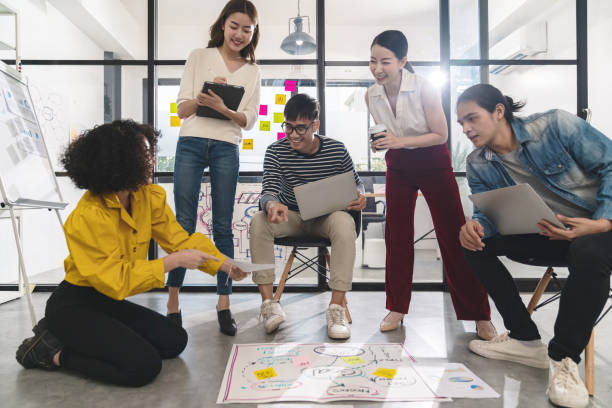 istock Young creative asian group meeting and looking at project plan lay out on floor discuss or brainstorm business strategy with post note. Workshop for startup team in small office. Happy workplace. 1207735815