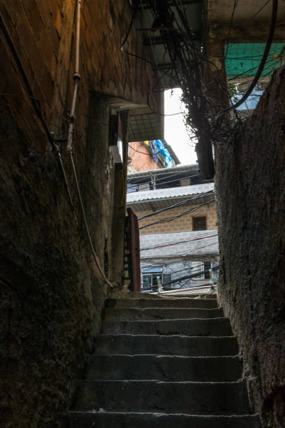 eine dunkle gasse mit stufen führt durch einen schmalen korridor zu einer städtischen straße in der rocinha favela in rio de janeiro, brasilien - rio de janeiro brazil steps staircase stock-fotos und bilder