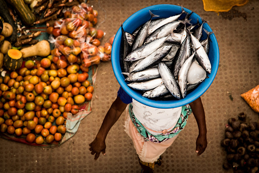 African woman carrying fish in a basket on her head on the local market in Assomada, Santiago.
