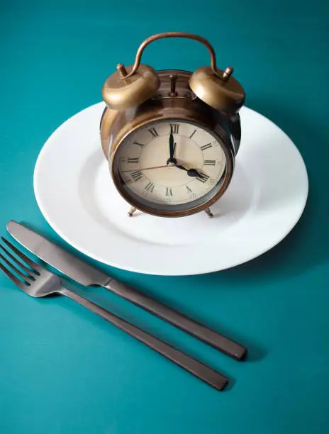 concept of intermittent fasting, ketogenic diet, weight loss. fork and knife on a plate and alarmclock