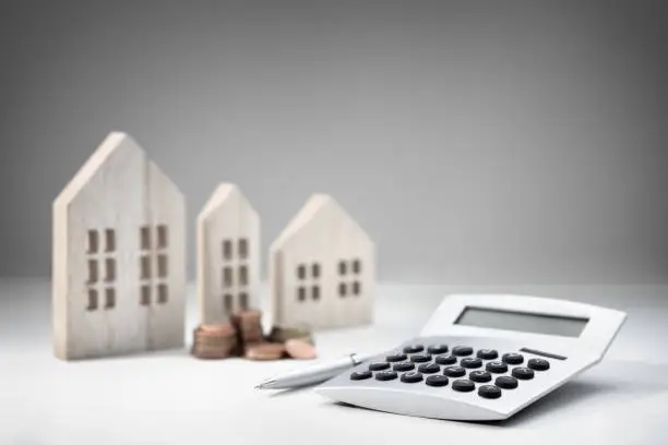 Photo of Calculator with wooden house and stack of coins