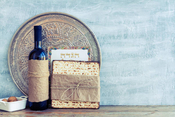 metal plate with matzah or matza and passover haggadah on a vintage wood background presented as a passover seder feast or meal with copy space. translation: passover haggadah - passover seder wine matzo imagens e fotografias de stock