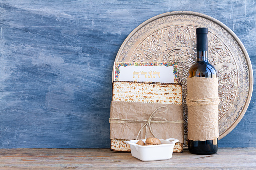 Metal plate with matzah or matza and Passover Haggadah on a vintage wood background presented as a Passover seder feast or meal with copy space. Translation: Passover Haggadah