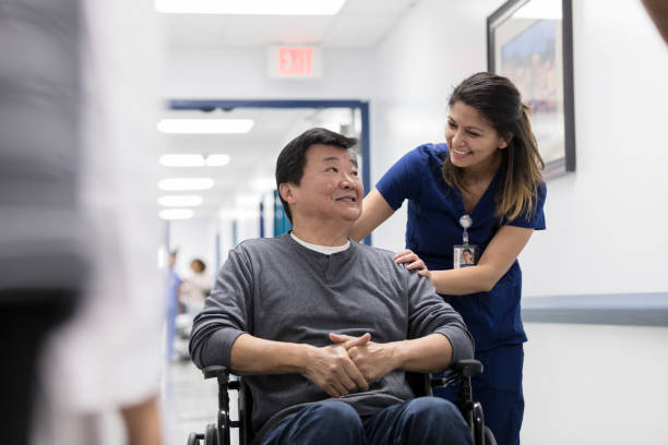 Cheerful nurse talks with senior patient Smiling senior man talks with a friendly nurse in a hospital hallway. The nurse is pushing the man in a wheelchair. goodbye stock pictures, royalty-free photos & images