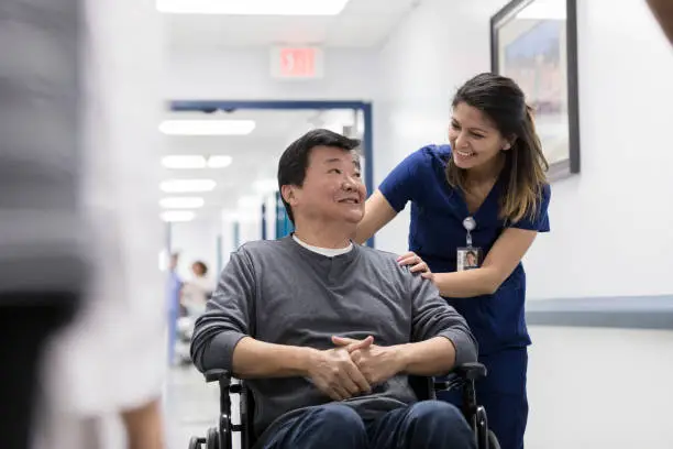 Smiling senior man talks with a friendly nurse in a hospital hallway. The nurse is pushing the man in a wheelchair.