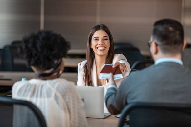 Female travel agent giving tickets to young happy couple. Female travel agent giving tickets to young happy couple. Photo of female travel agent and young couple. Young woman giving tickets and passport with visa to tourists. travel agency stock pictures, royalty-free photos & images