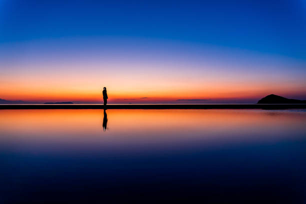 Silhouette of a male and walking at the seashore contemplating the moon valley in the water with Mountain View during twilight in Scandinavia