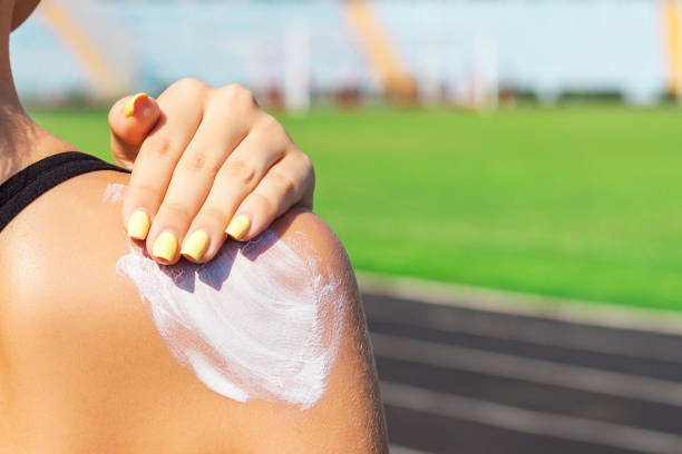 在體育場訓練之前，健身女郎正在肩上塗抹防曬霜。在體育活動中保護皮膚 - 防曬油 個照片及圖片檔