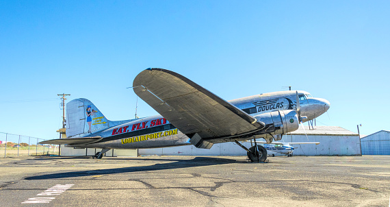 Lodi, California, USA - June 15, 2017: Antique Douglas DC-3 aircraft on the runway of an old airfield in Lodai, California, USA. The shiny fuselage of the plane against the background of hangars and a clear blue summer sky. History of American Aviation and Aircraft Engineering