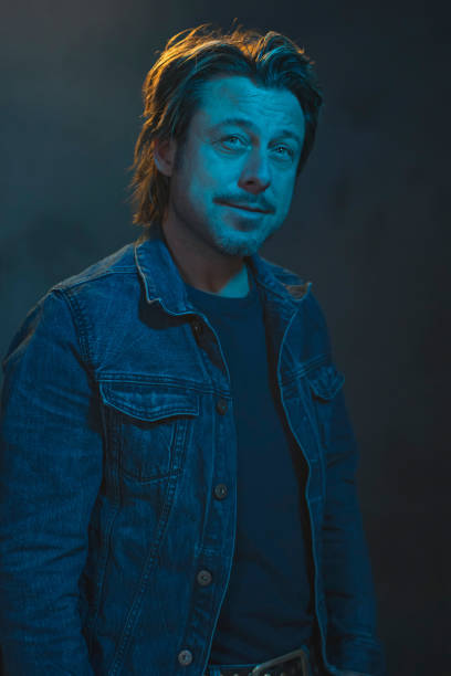 istock Smiling man in a blue denim jacket illuminated by blue and yellow light. 1207773535