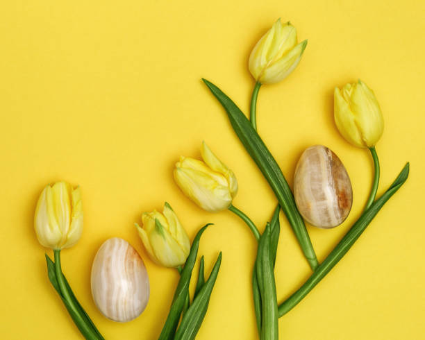 istock Pattern from decorative Easter eggs made from natural gemstone onyx and spring flowers of tulip on yellow backdrop. Trendy holiday greeting card. 1207775099