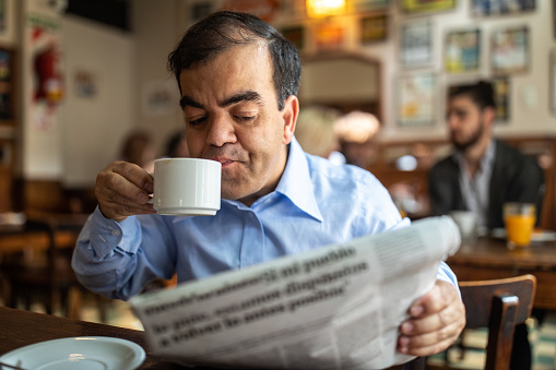 Businessman with dwarfism sitting alone in local cafe, reading newspapers and drinking coffee after work