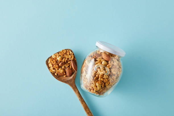 top-ansicht des glases granola mit holzspachtel auf blauem hintergrund - jar oatmeal granola glass stock-fotos und bilder