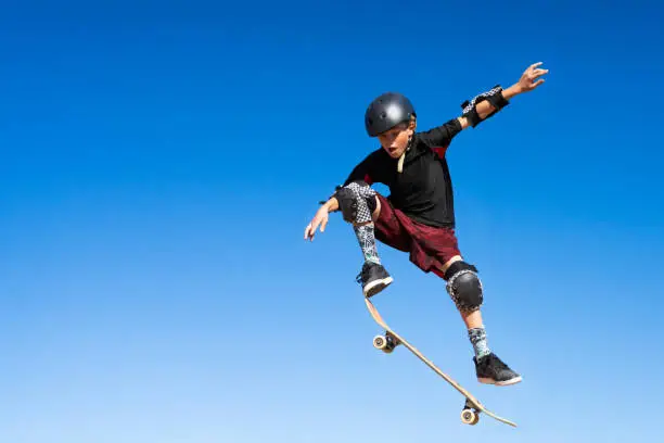 Young Boy on A Skateboard Jumping Into the Air.  Isolated on the blue sky.