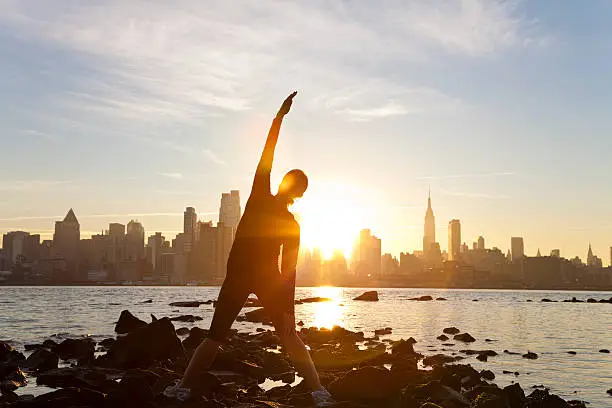 A woman runner stretching in a yoga position in front of the Manhattan skyline, New York City, United States of America, at early morning dawn sunrise