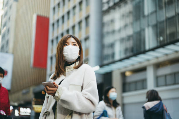 Young Asian woman with smartphone wearing a protective face mask to prevent the spread of germs and viruses in the city Young Asian woman with smartphone wearing a protective face mask to prevent the spread of germs and viruses in the city avian flu virus photos stock pictures, royalty-free photos & images