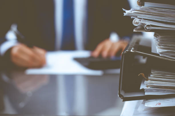 istock Binders with papers waiting to be processed with businessman or bookkeeper back in blur. Accounting planning budget. Audit, insurance and business concept 1207793582
