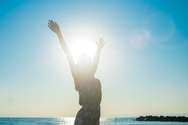 hipster young girl with outstretched hands standing in dress on the beach, the sun and sky background, back view