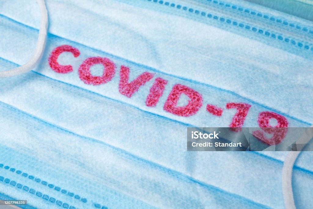 Blue Medical Disposable Face Mask with covid-19 printed on it. Covid-19 - Wuhan Novel Coronavirus pneumonia gets official name from WHO: COVID-19. Disposable breath filter face mask with earloop Covid-19 - Wuhan Novel Coronavirus pneumonia gets official name from WHO: COVID-19. Disposable dressing on the face. Healthcare background. Blue medical disposable face mask with covid-19 print China - East Asia Stock Photo