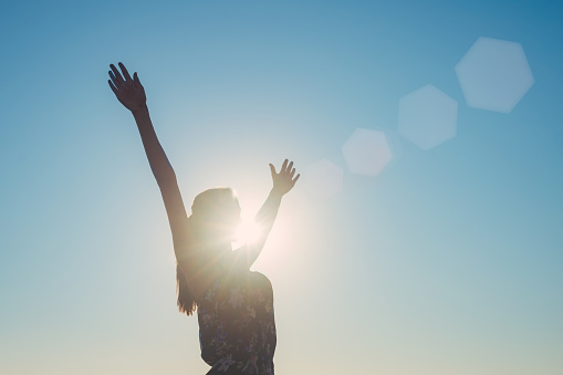 Silhouette of a girl with arms wide spread, the sun, rays and sky background