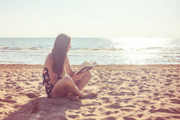 istock Girl reading book on sandy beach 1207798617
