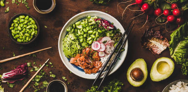 Salmon poke bowl with vegetables, greens, sushi rice, wide composition Healthy lunch, dinner. Flat-lay of salmon poke bowl or sushi bowl with vegetables, greens, sushi rice, soy sauce over rusty table background, top view, wide composition. Traditional Hawaiian cuisine foxys_forest_manufacture stock pictures, royalty-free photos & images