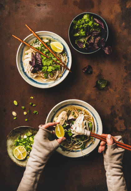 Womans hands with chopsticks and lime and vietnamese Pho-Ga soup