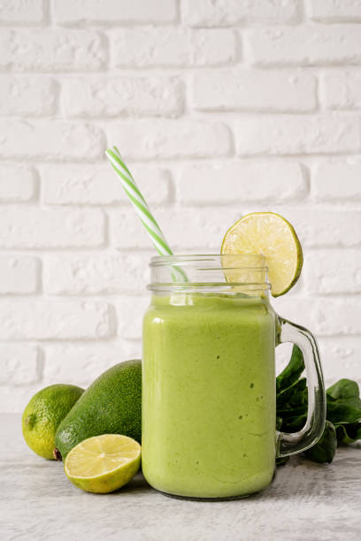 istock Avocado and spinach smoothie in mason jar front view on white brick wall background 1207805752