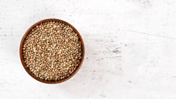 istock Small wooden cup with cannabis seeds on white stone like board - space for text right side 1207807279
