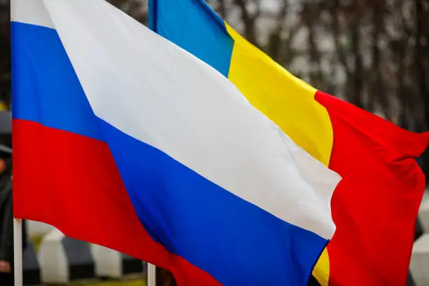 Romanian and Russian flags wave one next to another outdoors during a cold rainy day.