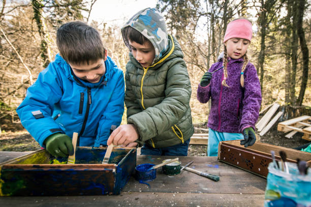 istock Young kids using paintbrushes to paint wooden boxes 1207817103
