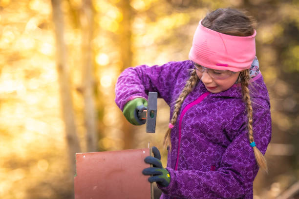 Young girl hammering a nail into a wooden box Photo of a young girl hammering a nail into a piece of wood. girl with a hammer stock pictures, royalty-free photos & images