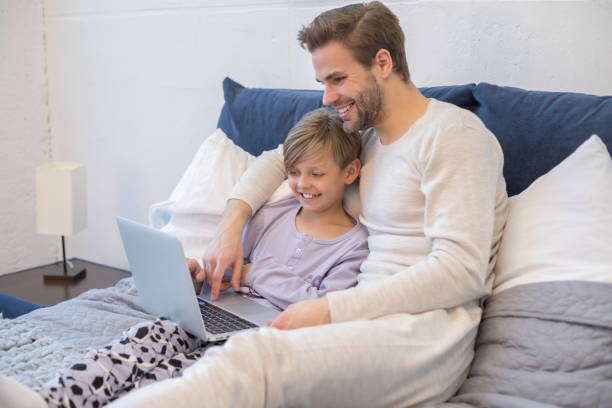 istock Smiling young man with his son typing on gadget in bedroom 1207822503