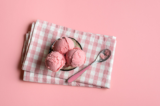 Raspberry ice cream in a glass bowl on napkin, on pink seamless background. Above view of berries ice cream.  Homemade red ice cream. Summer dessert.