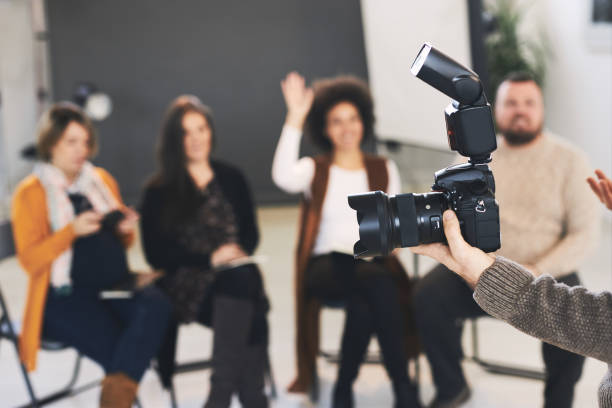 istock Closeup of tutor holding camera and explaining to attendees basics about photography. 1207824379