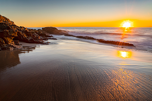 Long exposure photo of Sun setting over the ocean beach landscape at Thousand Steps Beach in Laguna Beach, Southern California, Orange County, California.