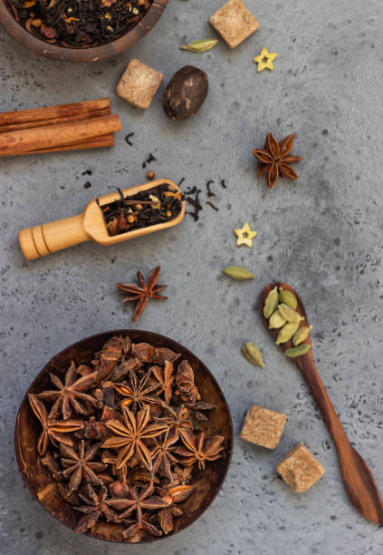 Photo of Ingredients for making spicy Indian masala chai tea or coffee. Dried black tea, roasted coffee beans, dry anise star seeds, cinnamon sticks, cardamom, black pepper and brown sugar.