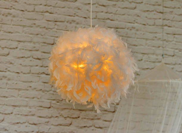 Modern lamp with abajur made of white feathers, gives romantic light in bedroom